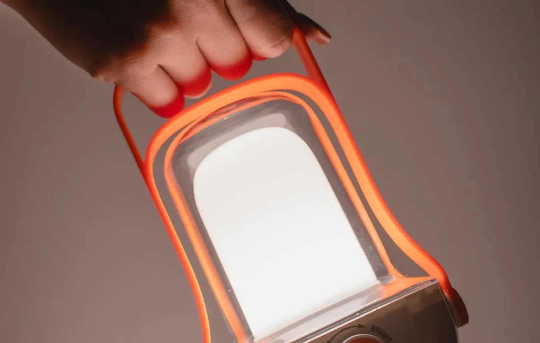 A hand holding an orange-framed electric lantern.