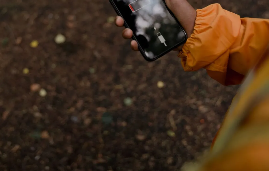 A hand holding a smartphone showing a low-battery screen outdoors.