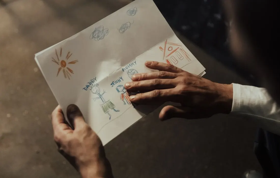 Hands holding a child's drawing of a family.