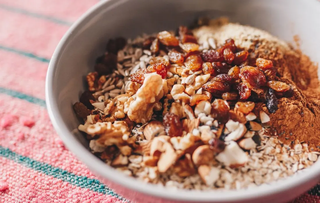 A bowl of oatmeal topped with nuts, seeds and raisins.