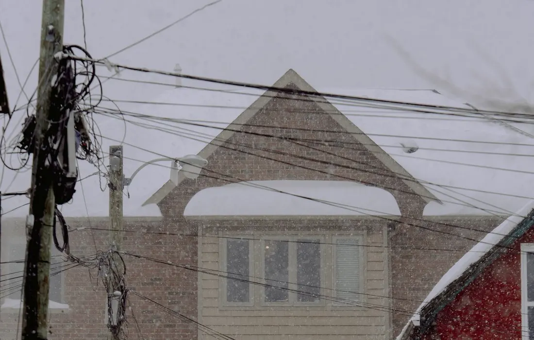A winter street scene with a snow-covered wooden house and falling snow.