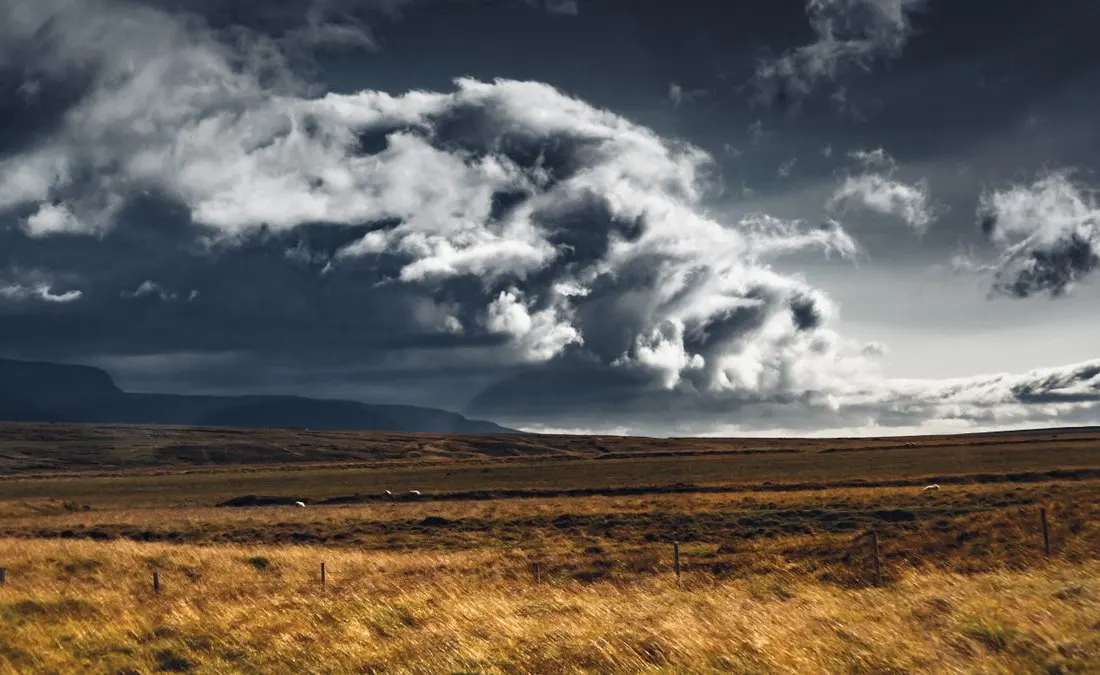Dark clouds above a broad field beside mountains.