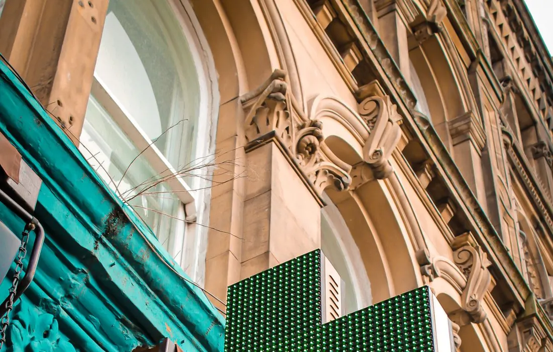 A green pharmacy cross mounted outside a building.