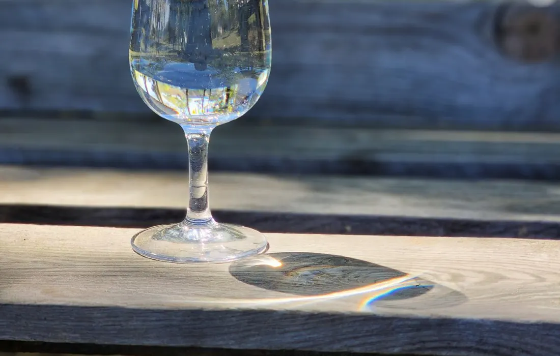 A glass of water on an outdoor wooden bench.
