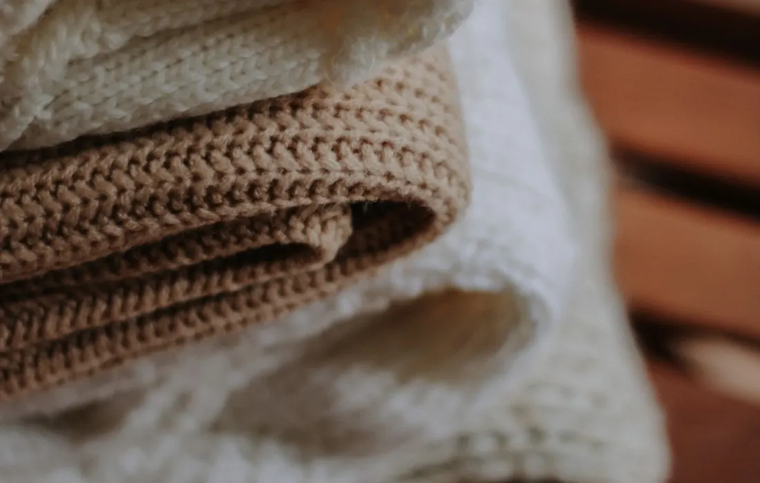 Close-up of neatly stacked beige and white wool blankets on a wooden chair.