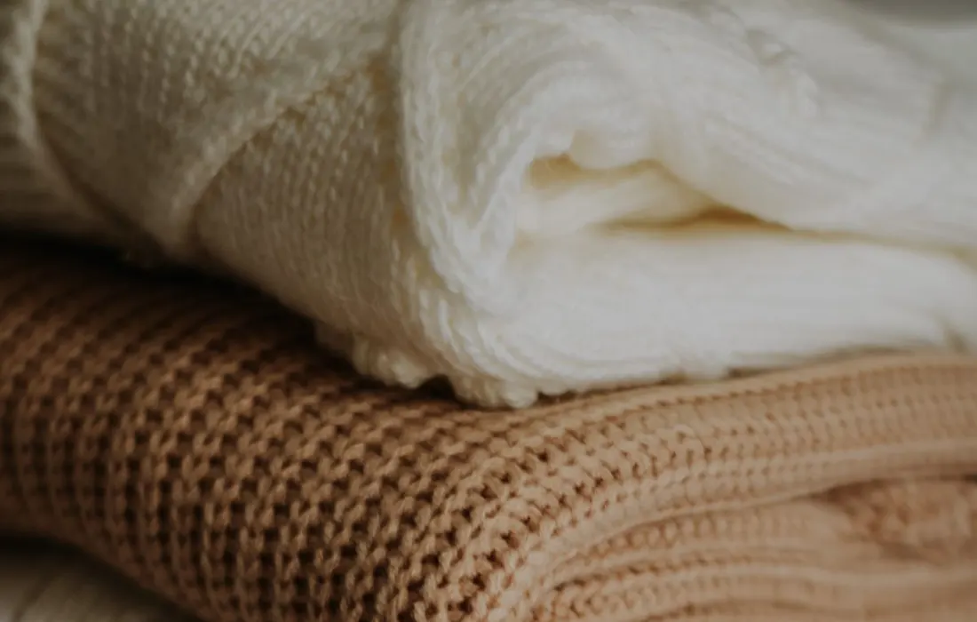 A stack of folded beige and cream knitted blankets.