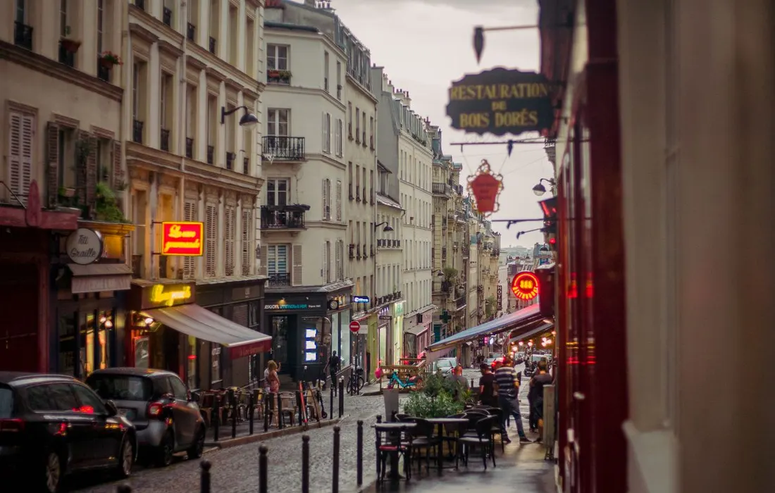 A wet cobbled street lined with Parisian buildings.