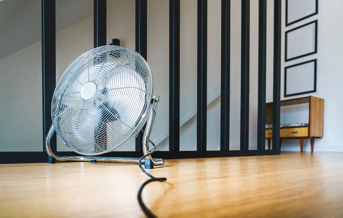 An electric fan standing on a wooden floor.
