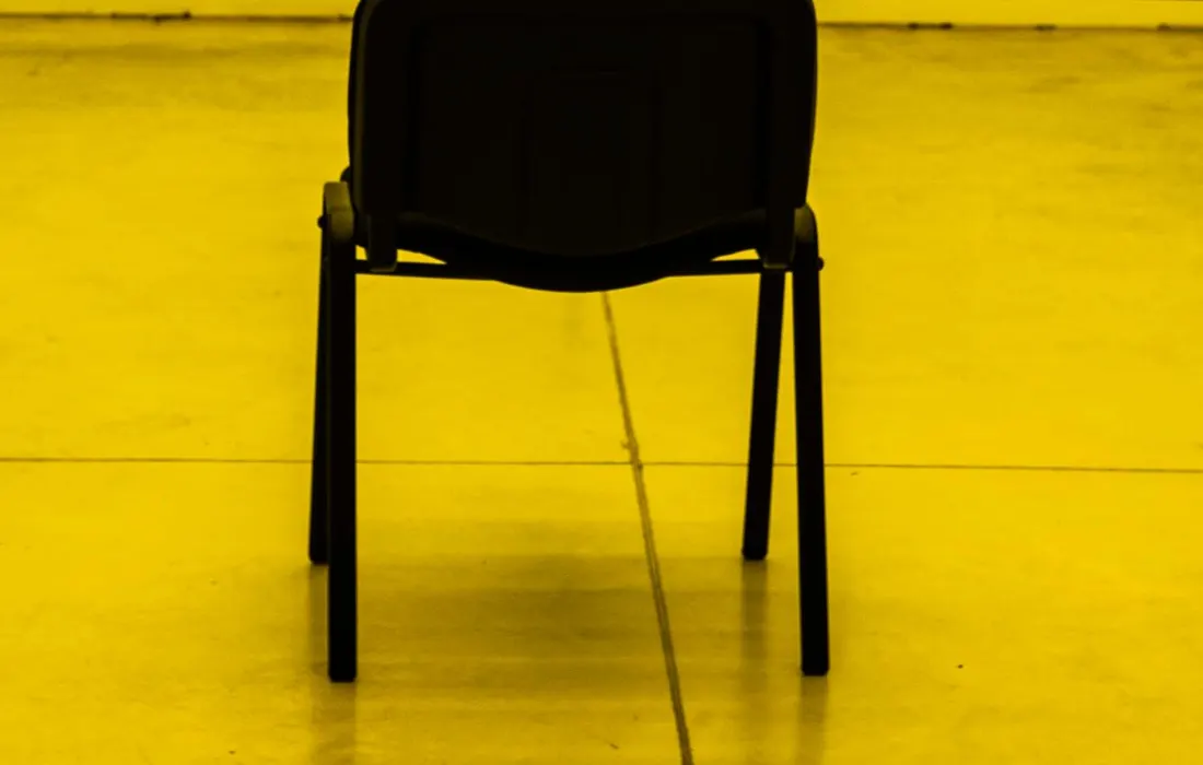 A black pedestal fan facing an empty chair.