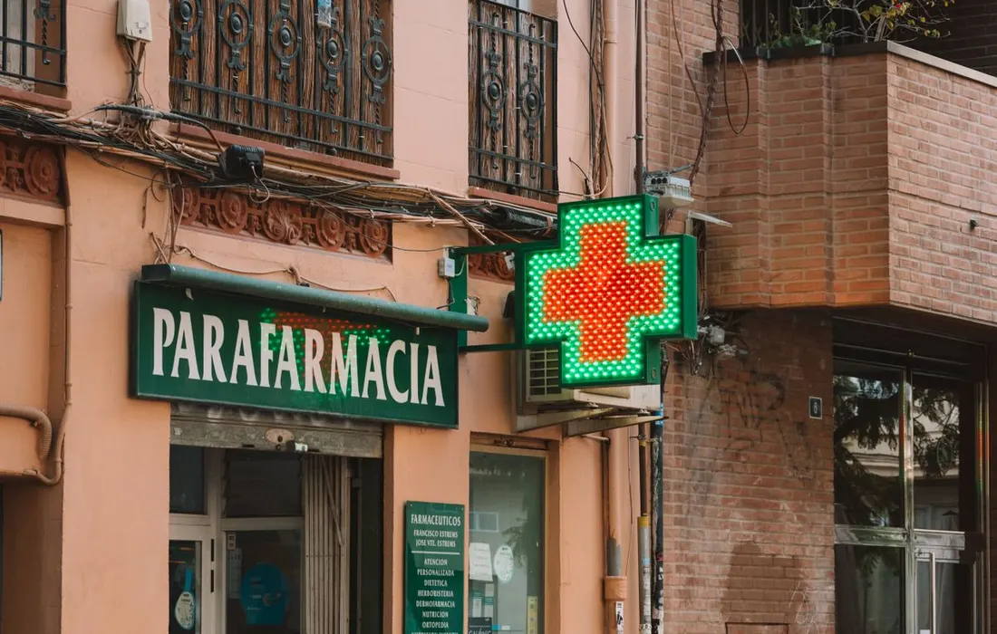 A glowing pharmacy cross outside a street-side building.
