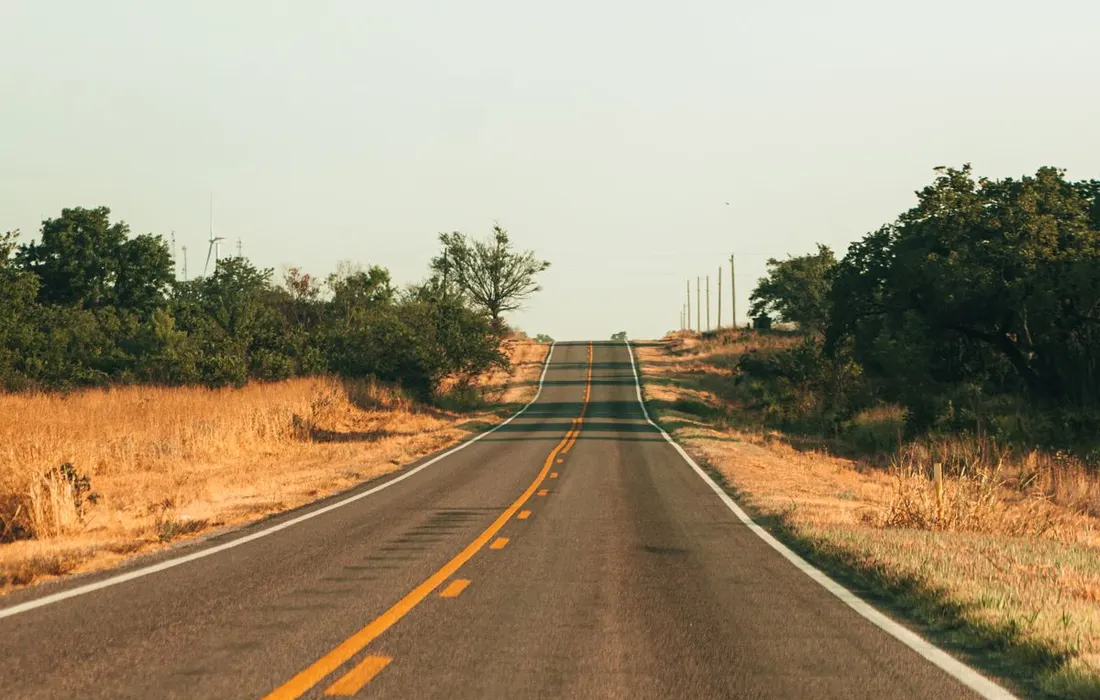 An empty asphalt road between dry summer fields.