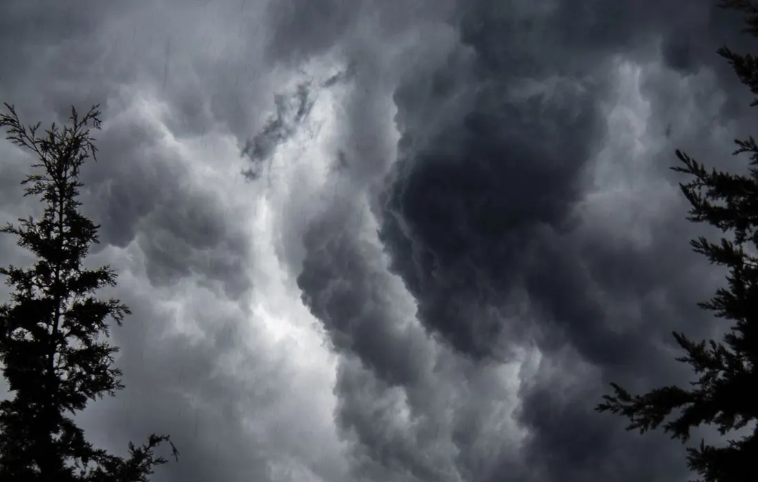 Rain clouds above a wooded landscape.