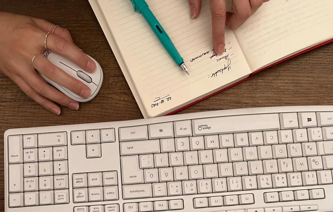 Hands writing a plan in a notebook beside a keyboard.