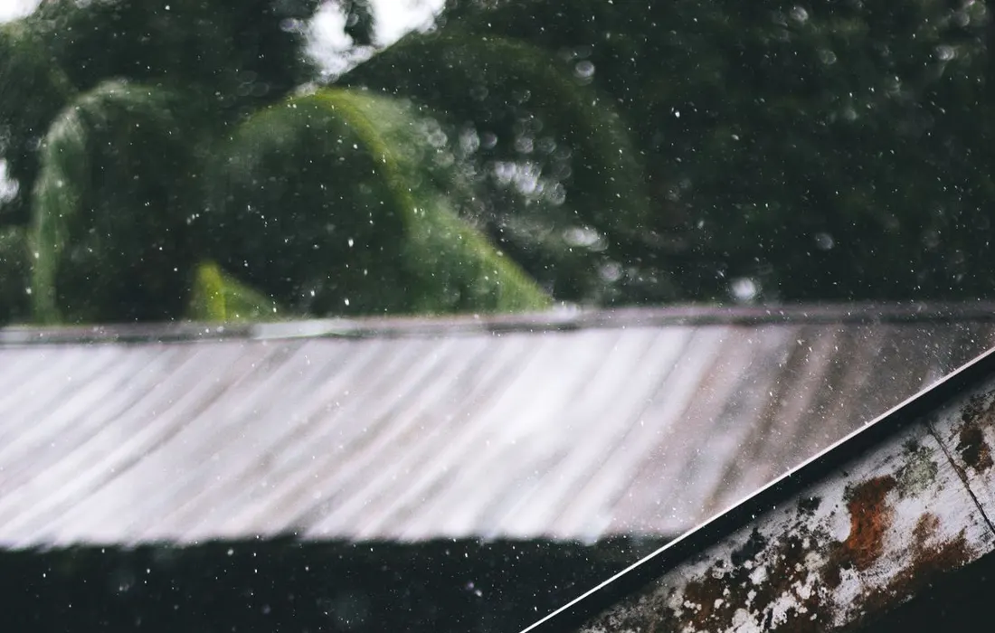 Glistening rain falls from a rusty metal roof, creating a moody, atmospheric scene.