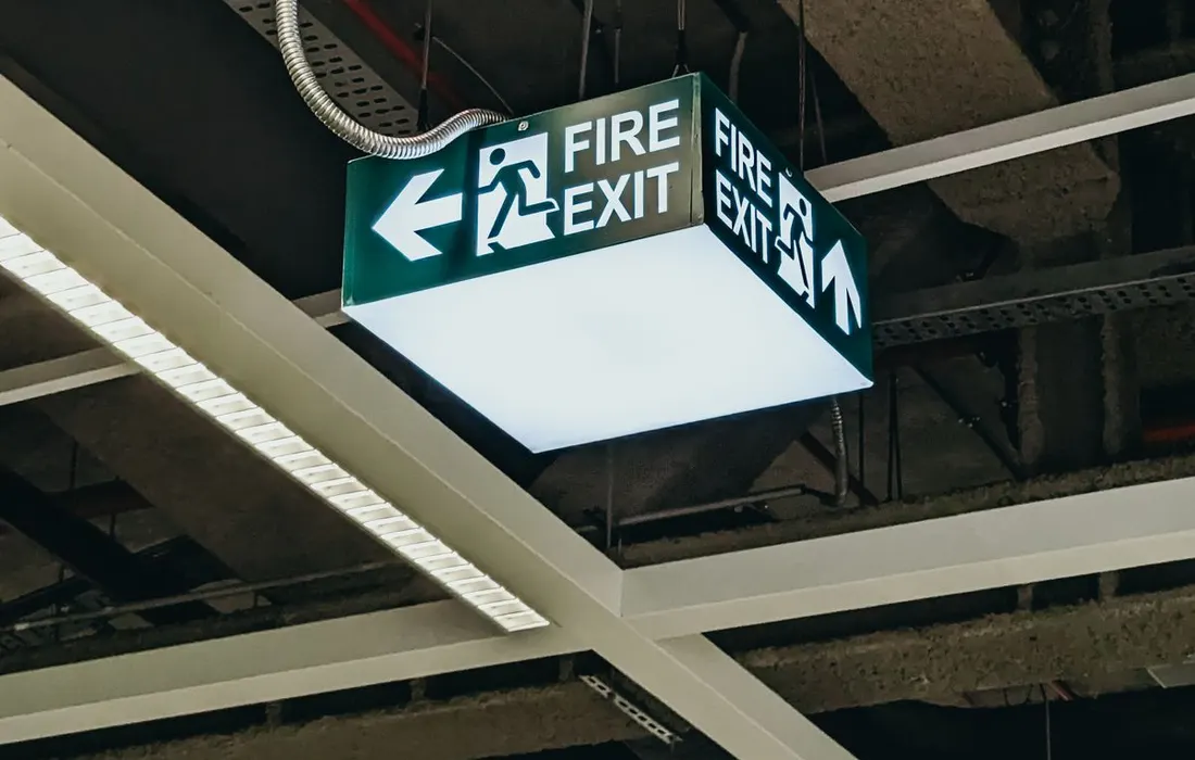 An illuminated emergency exit sign beneath a building ceiling.
