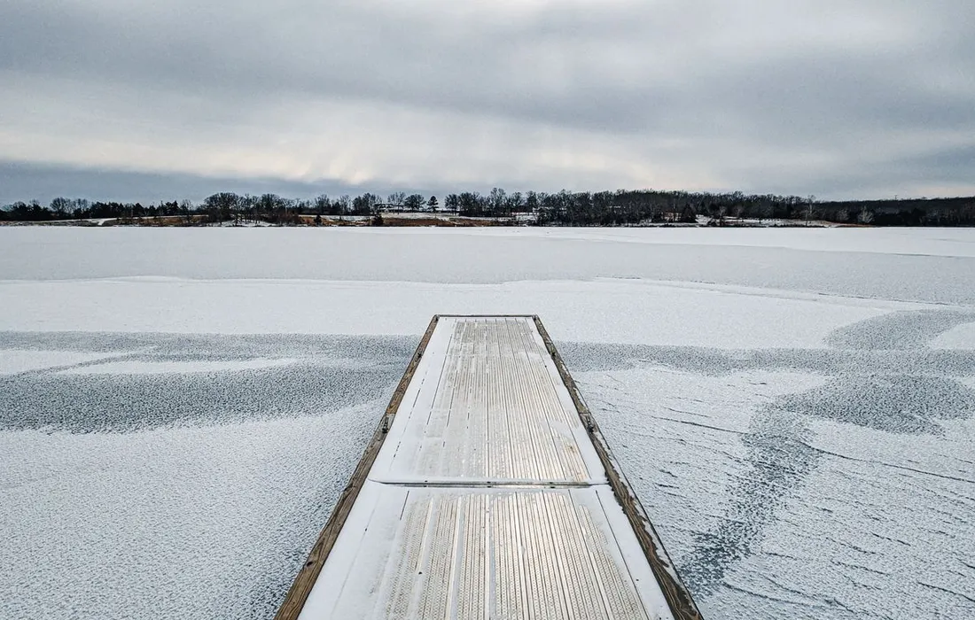 A serene and scenic view of a frozen lake with a wooden pier covered in ice during winter.