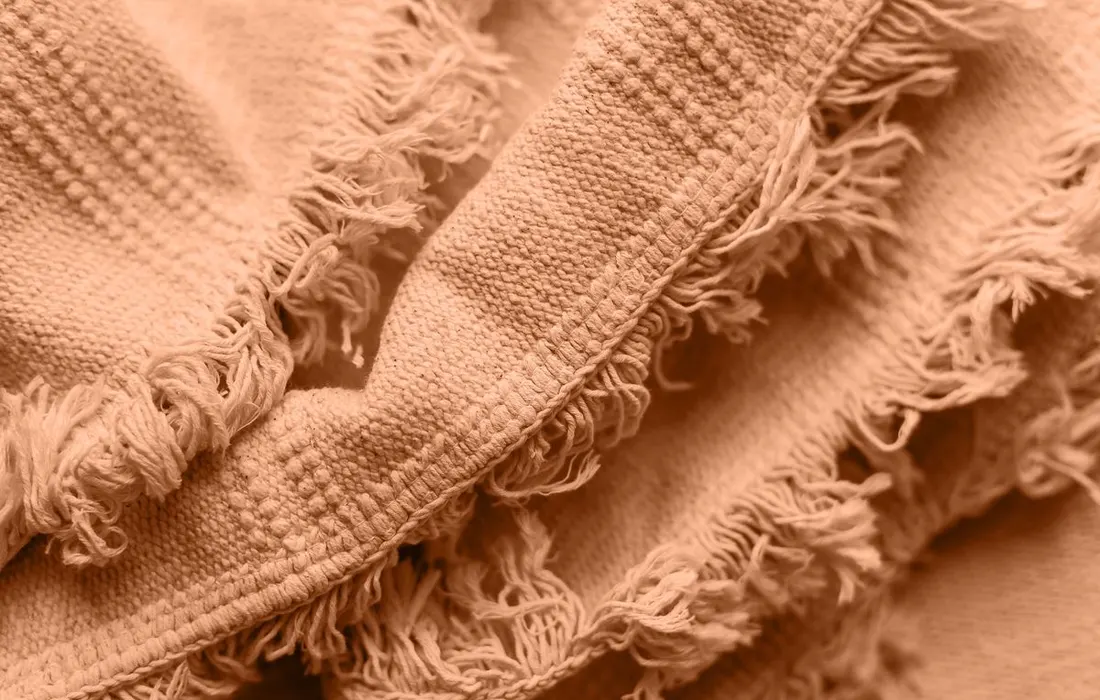 Detailed close-up shot of a soft woolen blanket with fringed edges, showcasing its textured weave.