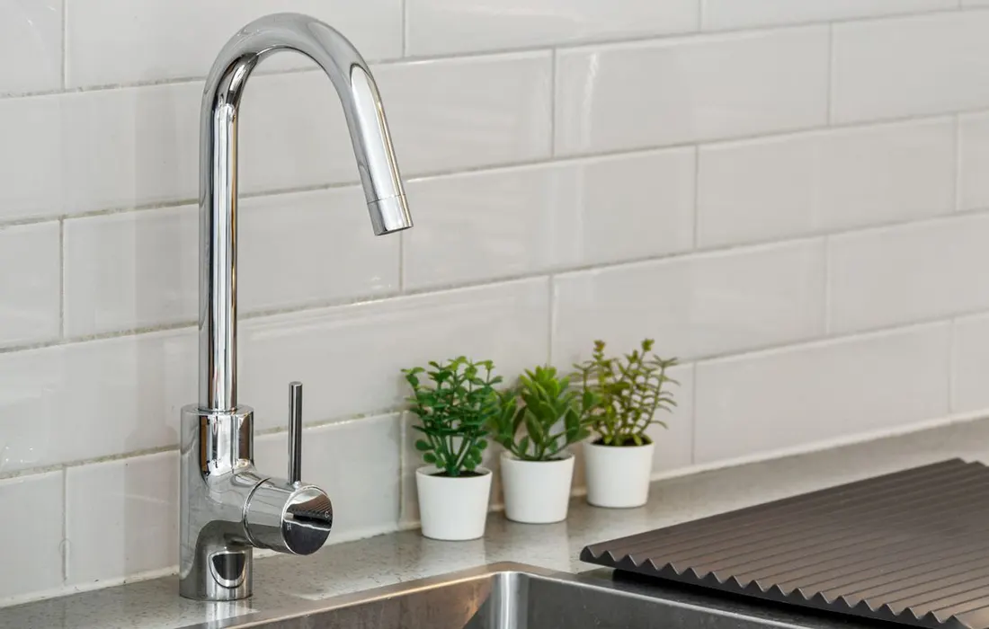 A kitchen sink and tap beneath a tiled splashback.