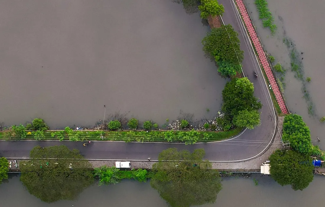 Top-down aerial view of a road partially submerged during a flood, surrounded by water and greenery.
