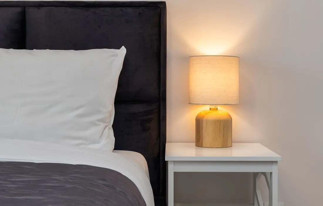 A lamp on a bedside table beside a bed.