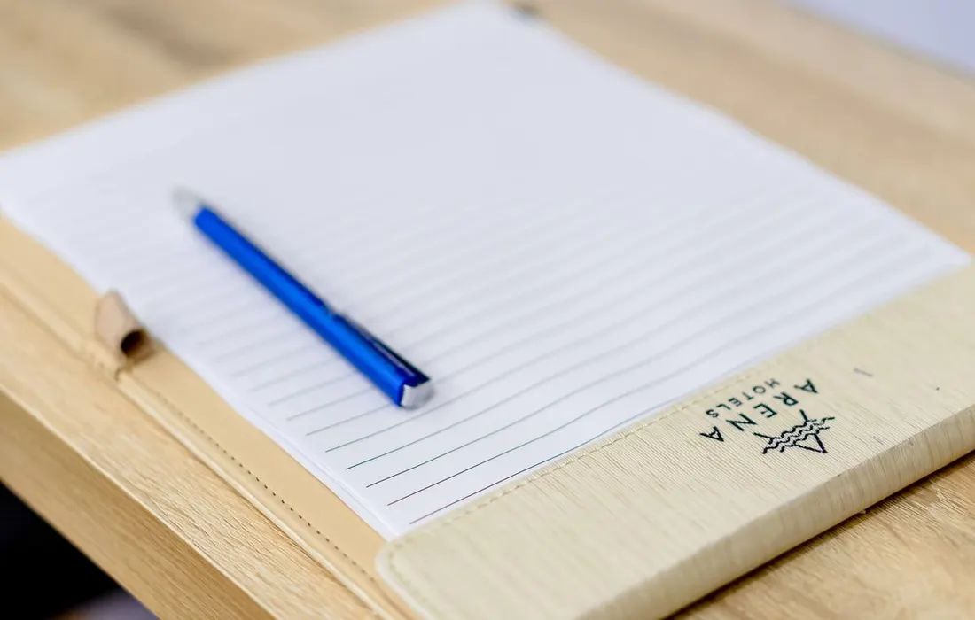 A pen resting on a lined paper notebook.