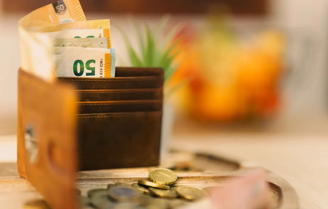 A wallet, banknotes and loose coins on a wooden table.
