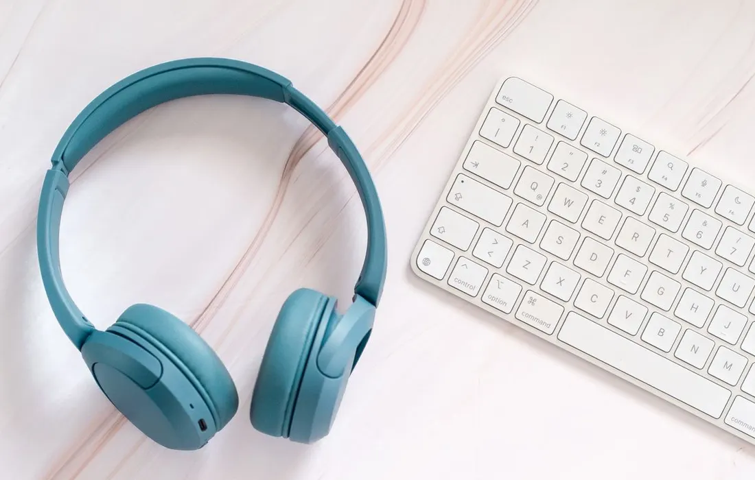 Headphones, a keyboard and a paper notebook on a desk.