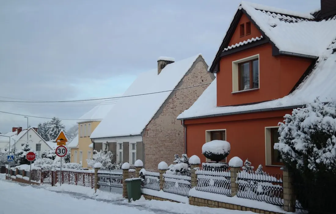 Charming snow-covered houses create a serene winter street scene with clear roads and fences.