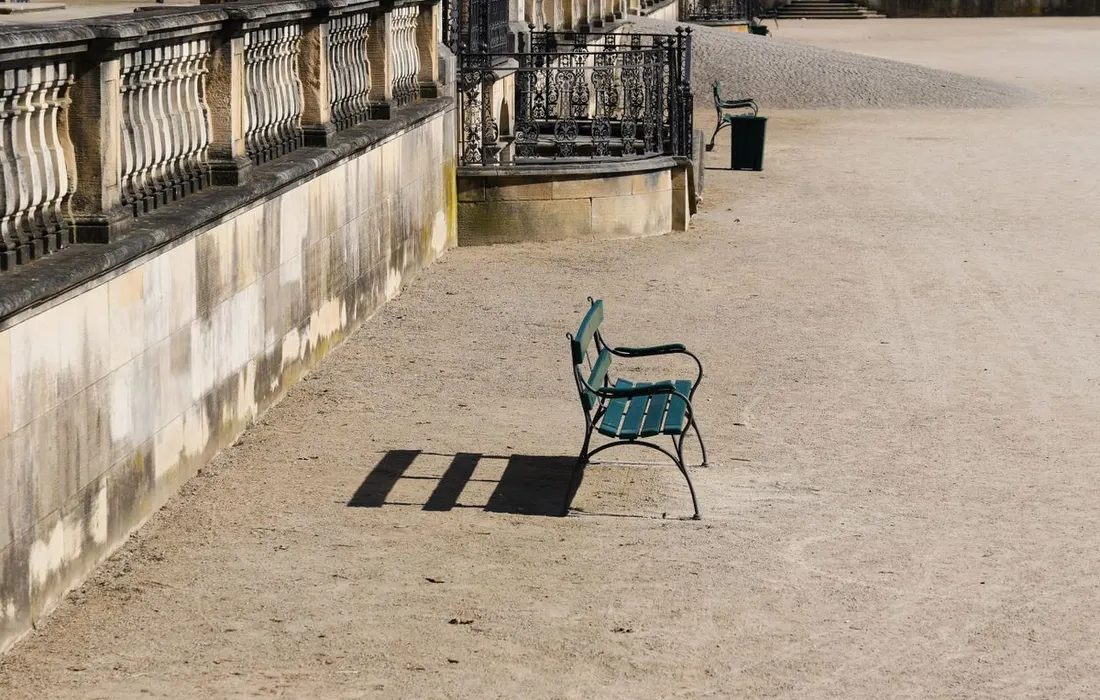 An empty bench casting shadows against a stone wall.