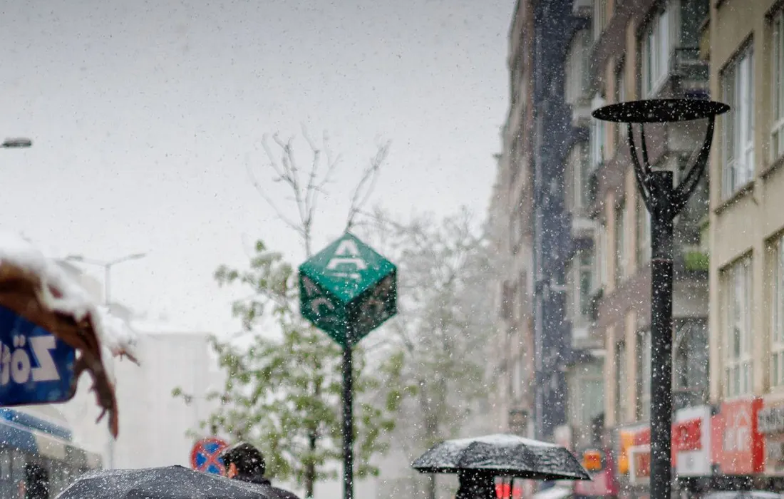 Pedestrians with umbrellas navigate a bustling city street during rainfall, showcasing urban life in adverse weather.
