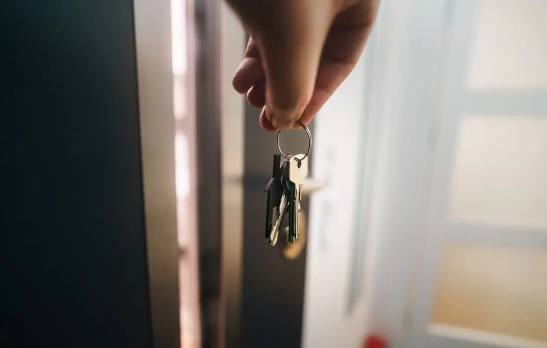 A hand holding house keys beside an open doorway.