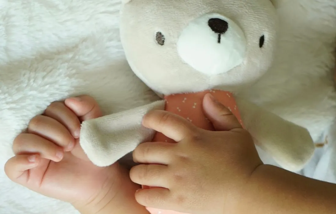 A child's hands holding a soft teddy bear on a blanket.