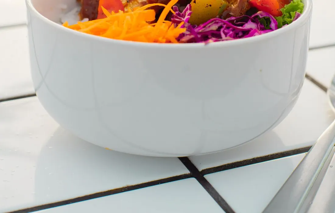 A bowl of fresh vegetables on a sunlit tiled table.