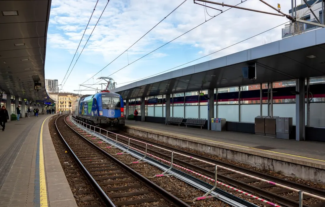A modern train beside an urban station platform on a clear day.
