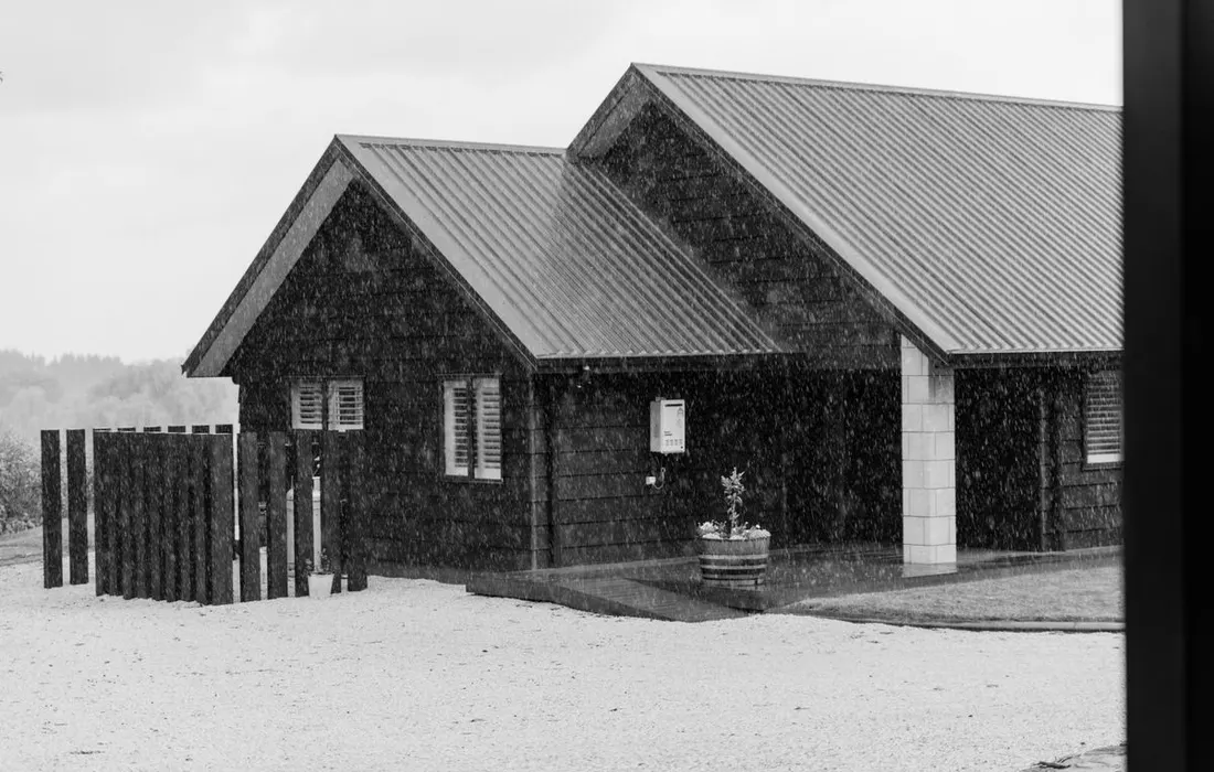 A black and white image of a wooden cabin in the rain, with a rustic feel.