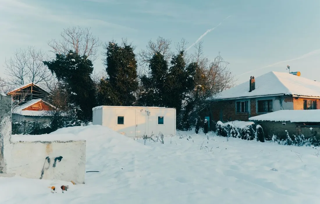 A serene snow-covered rural house during winter, showcasing a peaceful countryside scene.