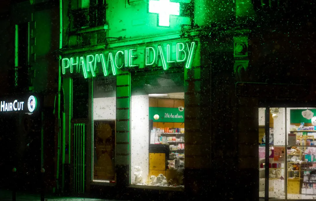 An illuminated green pharmacy sign at night.