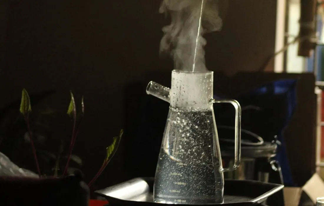 A kettle pouring steaming water into a glass jug.