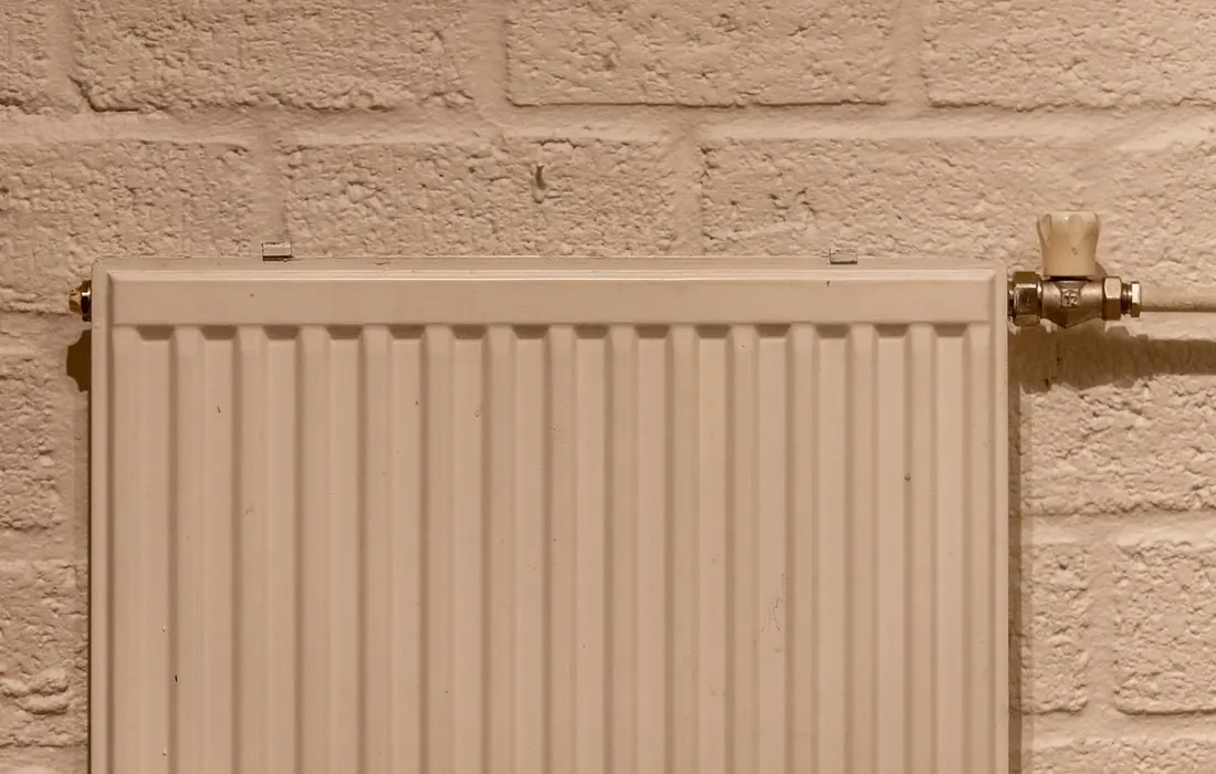 A white household radiator against a textured brick wall.