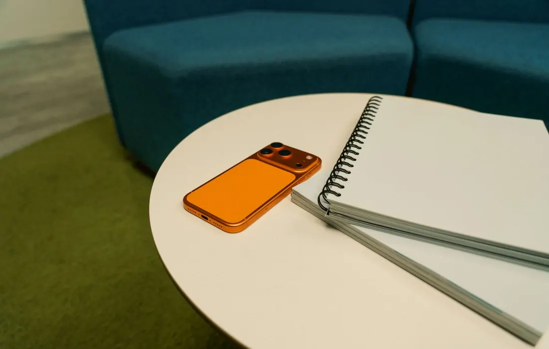 A smartphone and spiral notepad on a round table.