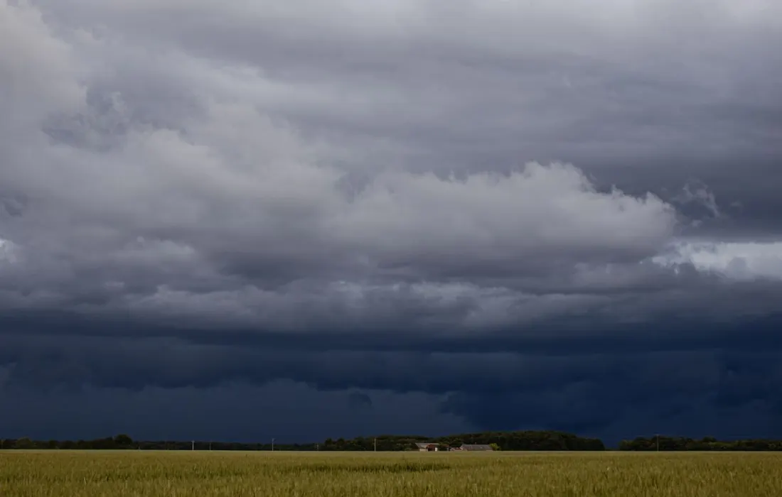 Storm clouds above fields and a farm landscape.