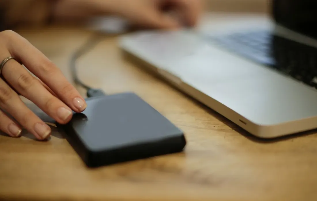 A hand connecting an external storage drive to a laptop.
