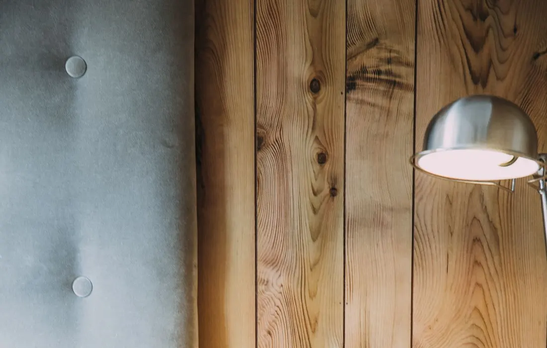 A bedside lamp and glasses on a table beside a bed.