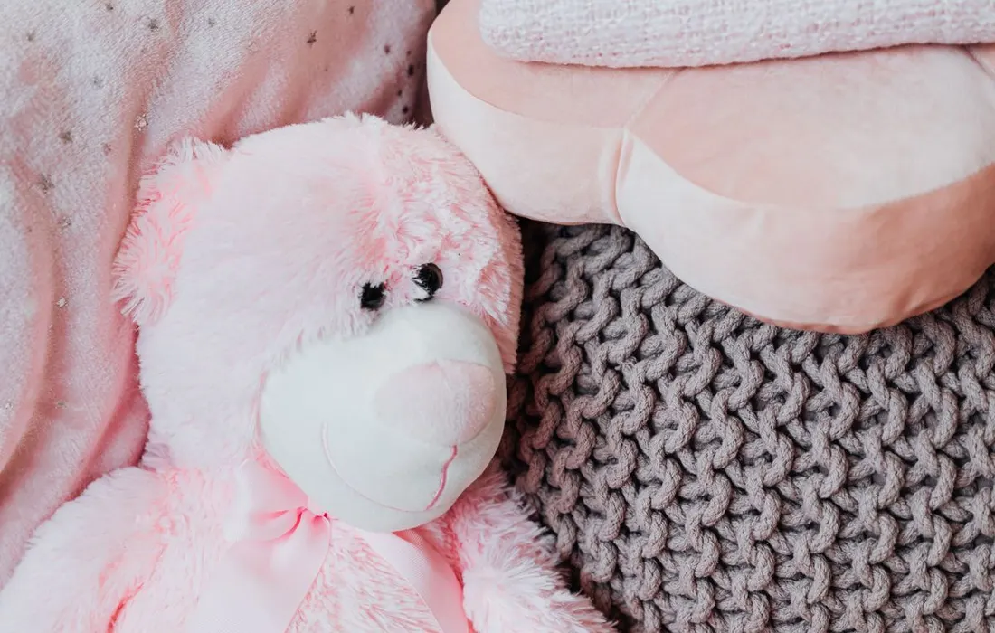 A pink soft toy resting on knitted fabric.
