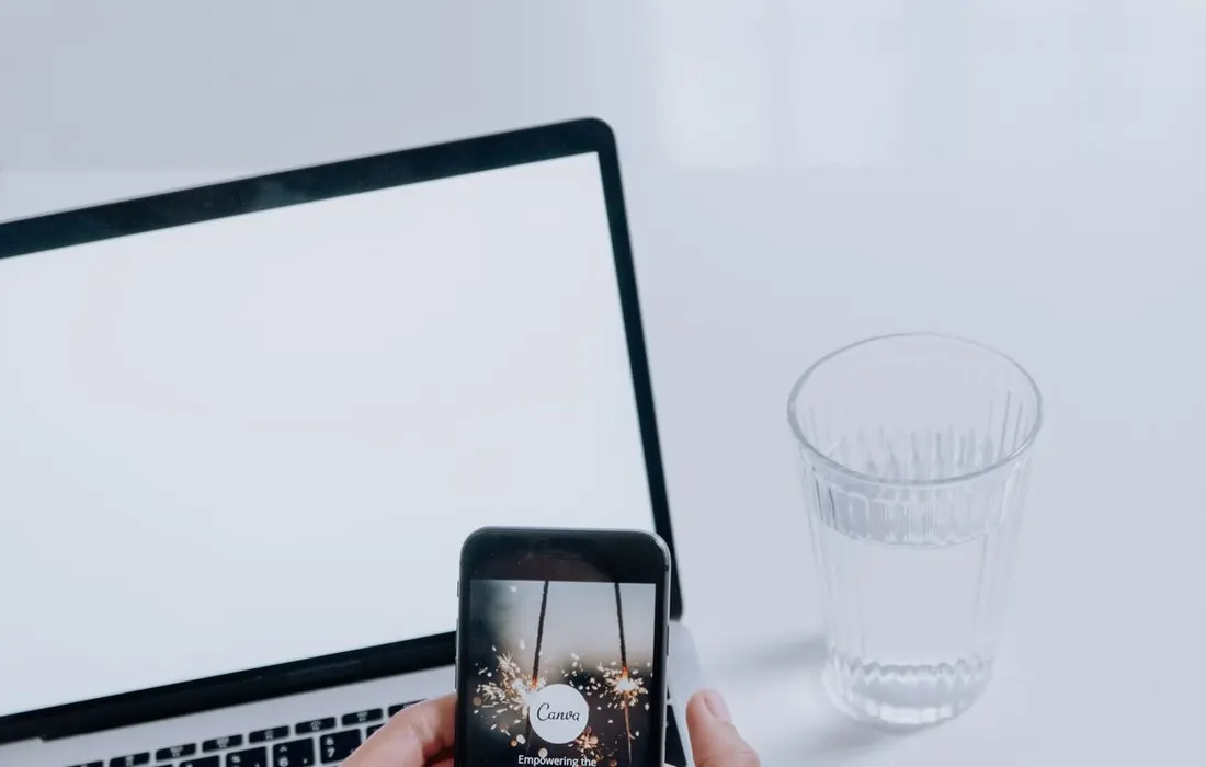 Hands holding a smartphone in front of a laptop.