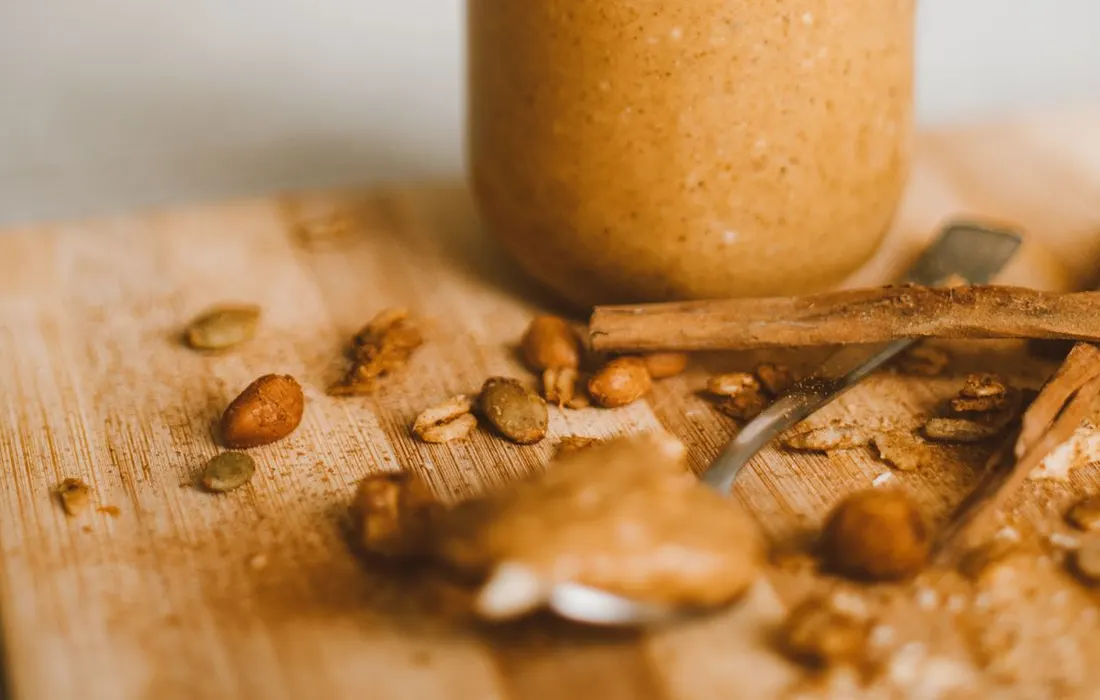 A jar of peanut butter with peanuts and seeds nearby.