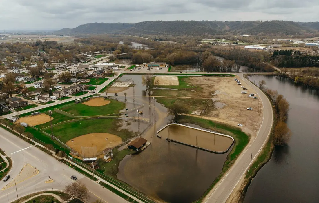 Aerial view of a flooded park area with baseball fields and roads during an overcast day.