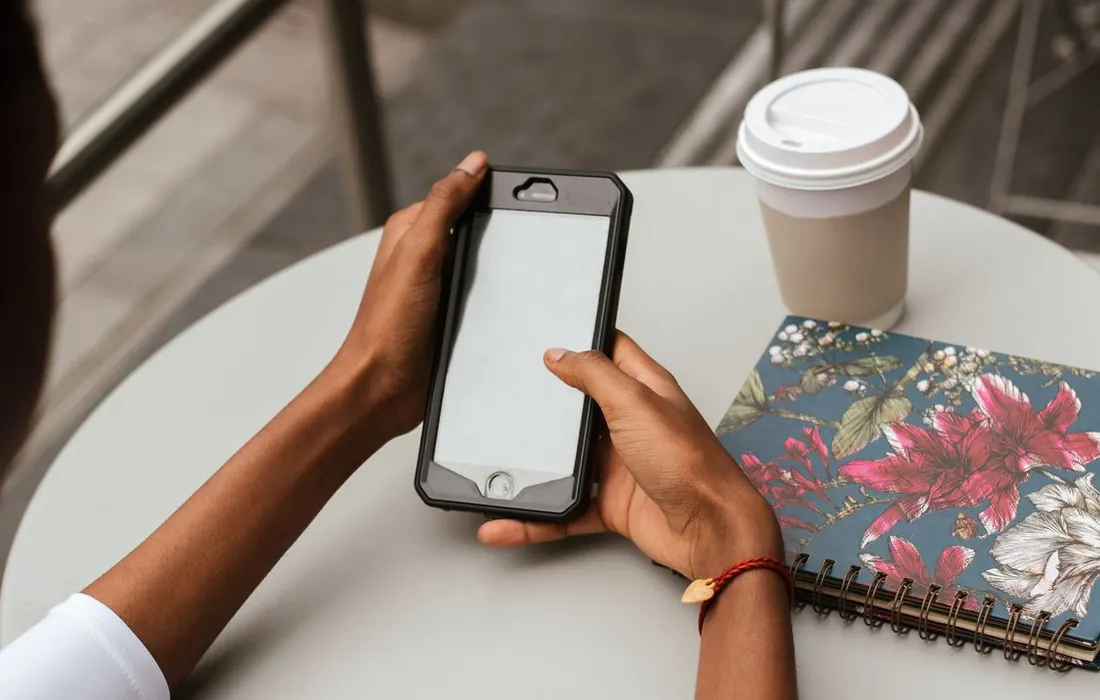 An anonymous person using a smartphone beside a notebook in a cafe.