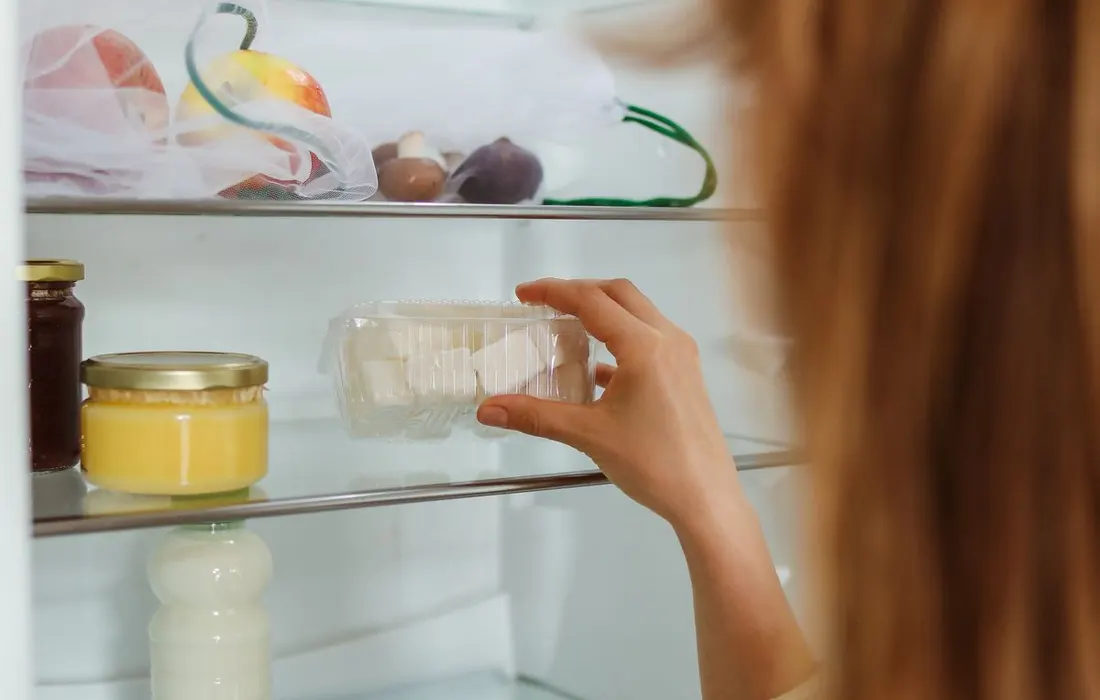 A hand reaching for food stored on refrigerator shelves.