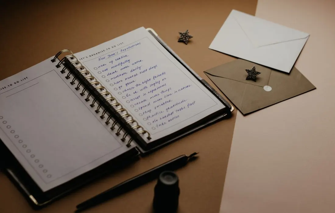 A paper planner, to-do list, envelopes and pen arranged on a desk.